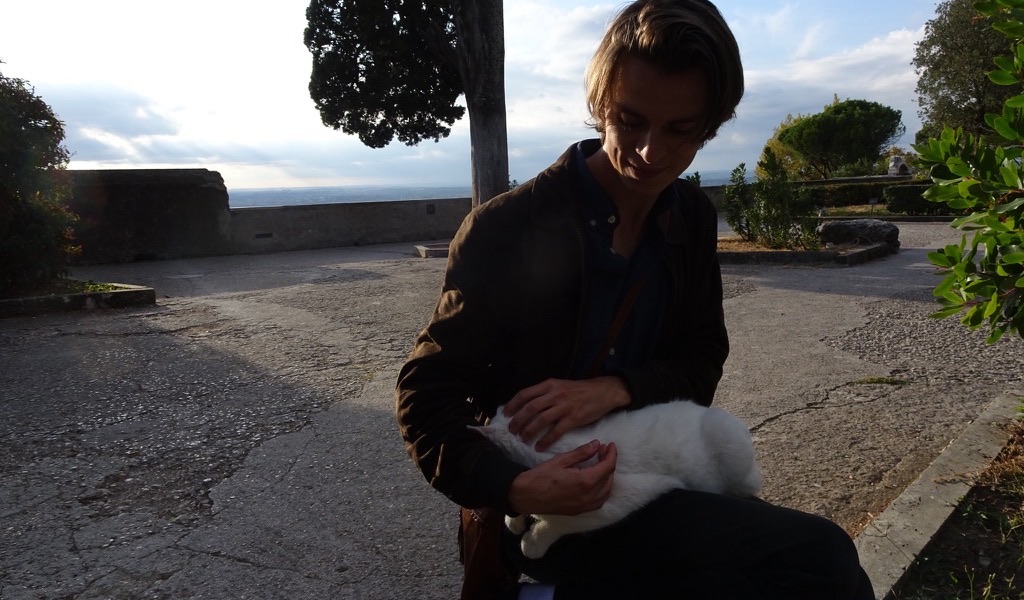 Aleksander Sekkelsten in Italy, holding a white cat on a hilltop terrace above the sea.