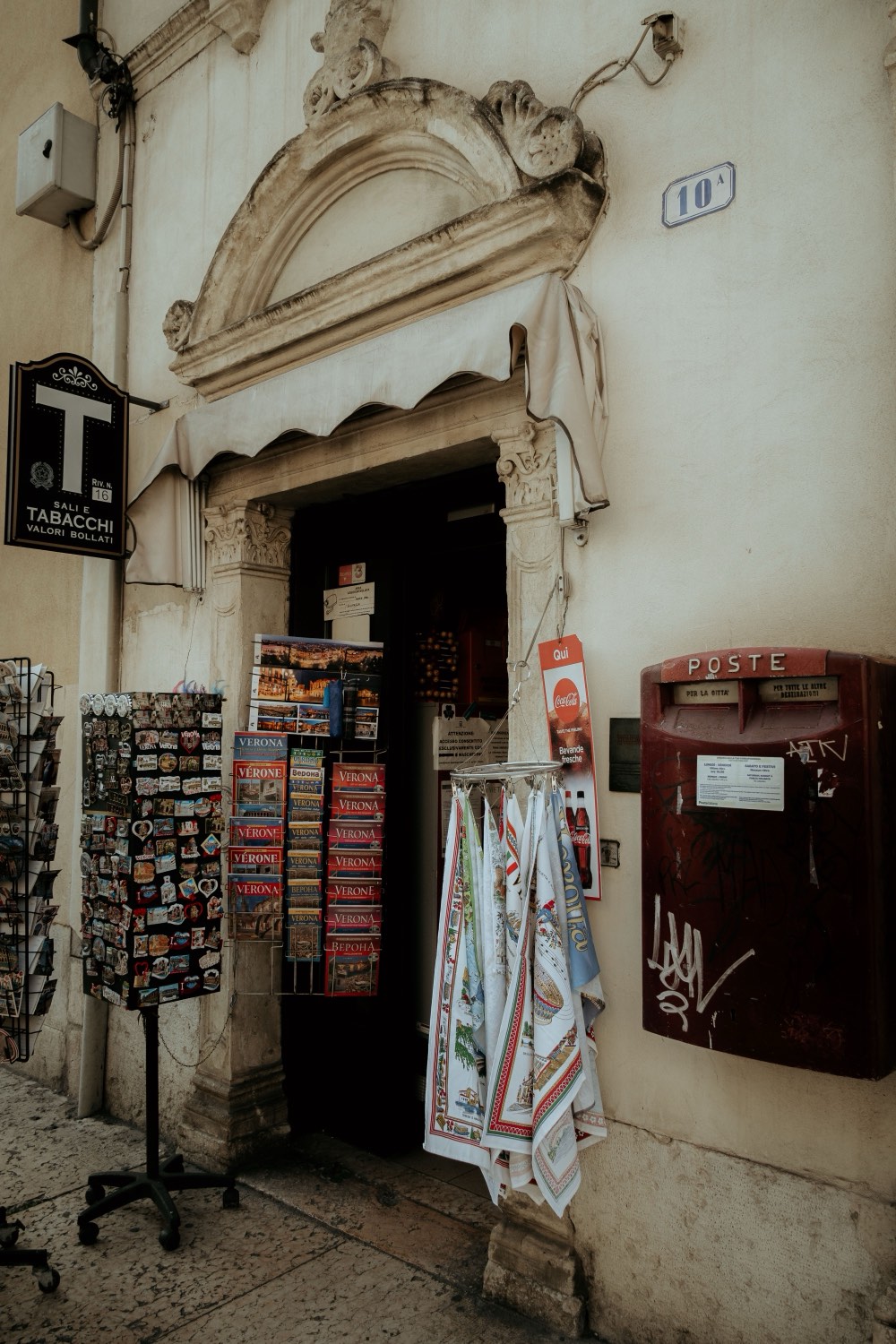 A sunlit Italian street with a small bar, a tabacchi sign, and people going about an ordinary morning.